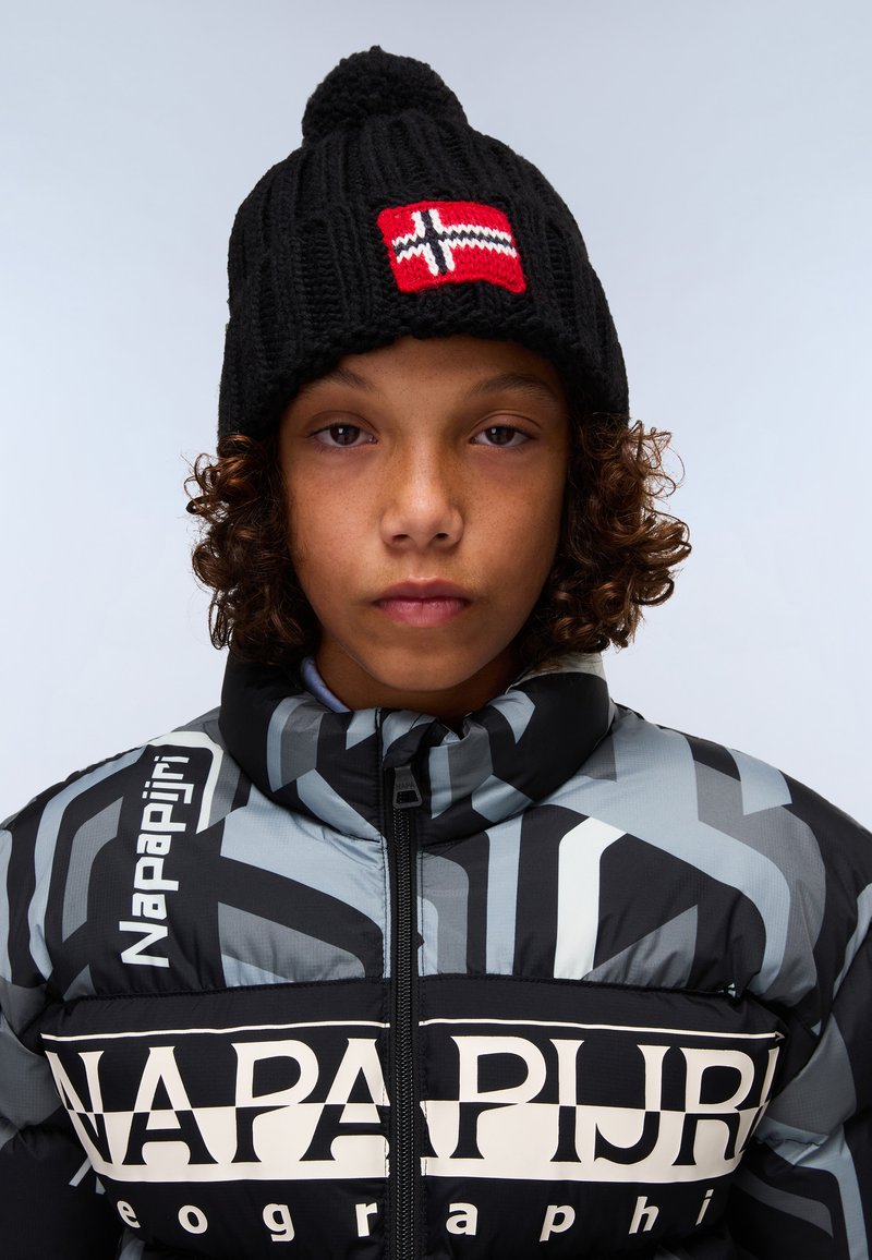 Svart stickad mössa med en röd och vit norsk flagga, bärs tillsammans med en svart och gråmönstrad pufferjacka med logotyp.