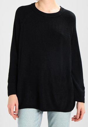 Schwarzer Pullover mit gerippter Struktur, lockerer Passform und weitem Ausschnitt, kombiniert mit hellblauen Jeans.