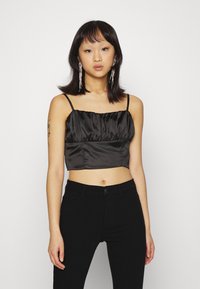 Top cropped de cetim preto com corpete franzido, alças finas ajustáveis e textura suave. Combinado com jeans pretos ajustados.