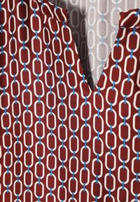 Rood patroonstof met witte en lichtblauwe kettingachtige schakels, met een V-hals en een gladde textuur.