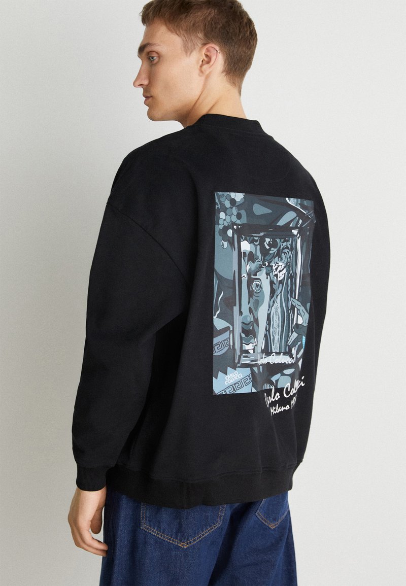 Zwarte sweatshirt met een grote grafische print op de rug met blauwe en witte illustraties. De stof lijkt zacht en textuur te hebben.