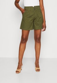 Shorts en coton vert olive avec taille haute, plis à l'avant et fermeture à trois boutons. Ils disposent de poches latérales et d'un ourlet droit.