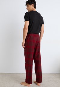 Pantalons de pyjama à carreaux rouges avec une coupe décontractée, une taille élastique et en coton. Assortis à un t-shirt noir uni, vus de dos.