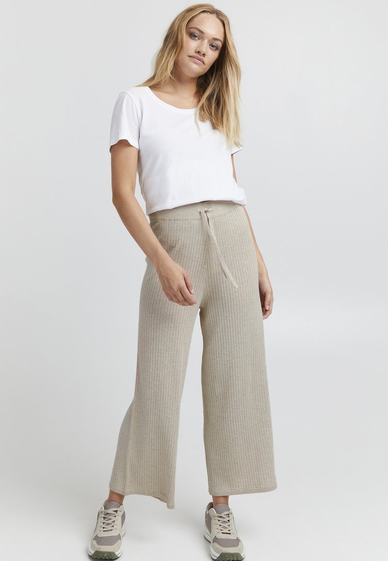 T-shirt bianco in cotone leggero abbinato a pantaloni larghi beige a coste con vita regolabile e finitura testurizzata.