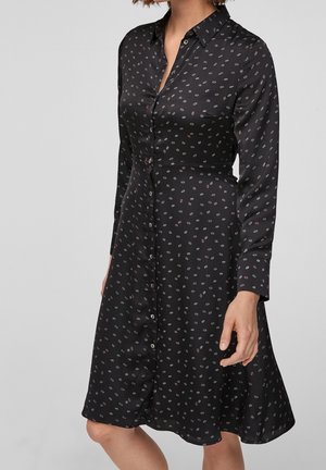Czarna sukienka zapinana na guziki z kołnierzykiem, ozdobiona kwiatowym wzorem w jasnych kolorach. Satynowa faktura, długie rękawy i rozszerzany dół.