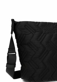 Bolso bandolera negro acolchado con correa ajustable y patrón de costura geométrica visto desde el lado.