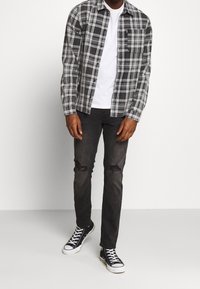 Camicia di flanella a quadri bianco e nero sopra una maglietta bianca, abbinata a jeans neri strappati e sneakers alte nere.