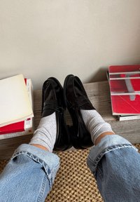 Black patent leather loafers with a raised seam detail, worn with gray crew socks; visible denim jeans with rolled cuffs.
