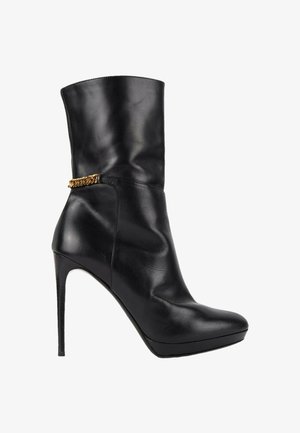 Botte mi-mollet en cuir noir à talon haut aiguillé avec un bout pointu et un fin talon stiletto, ornée d'un petit détail de chaîne dorée à la cheville.