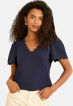 Marineblaue V-Ausschnitt-Bluse mit gewellten Ärmeln und bestickten Akzenten. Weicher Stoff, lockere Passform und dekorative Kante am Ausschnitt.