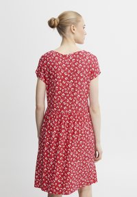 Punainen kukallinen mekko lyhyillä hihoilla, jossa on löysä istuvuus, rypistetty vyötärö ja pieniä valkoisia kukkakuoseja kankaassa.