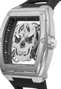 Srebrna ura iz nerjavečega jekla z dizajnom lobanje. Ima kristalne poudarke, črn gumijast pašček in pravokotno ohišje. Opazen je mehanizem zobnikov.