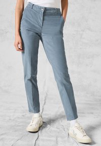 Lichtblauwe broek van een gladde stof, met een ritssluiting en knoopsluiting, met tapse benen en zijzakken. Gepaard met witte sneakers.