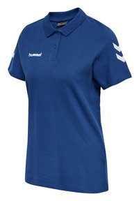 Blå polo shirt gjord av bomullsblandad tyg, med krage, korta ärmar och vita chevron akcentuer på axlarna. Logotyp på bröstet.