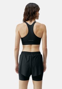 Melnā sporta krūštura un šortu komplekts ar racerback dizainu, elastīgu jostu un slāņainu izskatu ar gludu tekstūru.