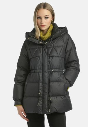Black insulated puffer jacket with a hood, featuring diamond quilting, drawstring waist, and gold-tone hardware. Worn over a green knit sweater.