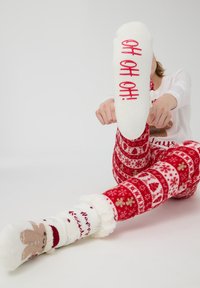 Białe wełniane skarpetki z czerwonym napisem "OH OH OH!", noszone z czerwonymi spodniami od piżamy w wzory z płatkami śniegu i świątecznymi motywami.