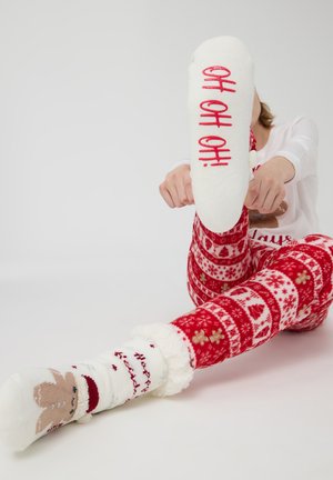 Białe wełniane skarpetki z czerwonym napisem "OH OH OH!", noszone z czerwonymi spodniami od piżamy w wzory z płatkami śniegu i świątecznymi motywami.