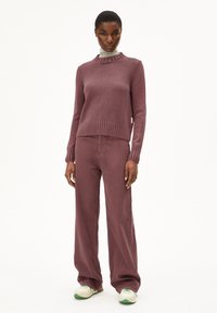 Lila gerippter Pullover mit hohem Kragen und Rüschendetails, kombiniert mit passenden weit geschnittenen Hosen und Sneakers mit grünen Akzenten.