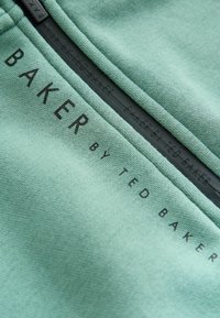 Mintgrüner Sweatshirt mit glatter Textur und einem schwarzen Etikett, auf dem "BAKER BY TED BAKER" in fetten Buchstaben gedruckt ist.