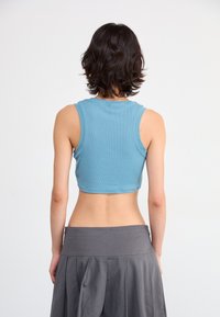 Light blue ribbed crop top with a high neckline and wide armholes, paired with a gray skirt featuring a pleated design and wide waistband.