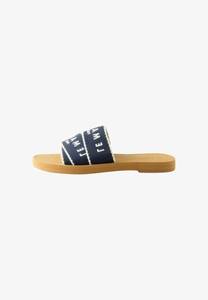 Flache Slides-Sandale mit brauner Sohle und breitem marineblauem Stoffriemen mit weißem diagonalen Text.