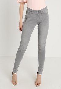 Graue Skinny-Jeans aus Stretch-Denim mit schlankem Schnitt und klassischem Fünf-Taschen-Design, kombiniert mit einem hellrosa Oberteil.