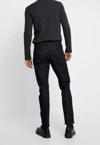 Jeans de mezclilla negra con corte ajustado, que presentan un diseño clásico de cinco bolsillos, un sutil detalle de costura y un acabado en tela texturizada.