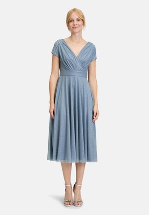 Himmelblaues knielanges Kleid mit V-Ausschnitt, kurzen Ärmeln, gefaltetem Oberteil und glitzernder Textur. Kombiniert mit silbernen Riemchen-High Heels.