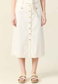 Valkoinen denim-hame polvipituudella, jossa on edessä napituskiristys, kaksi etutaskua ja vyötäröllä sidottava vyö. Teksturoitu kangas ja siisti muotoilu.
