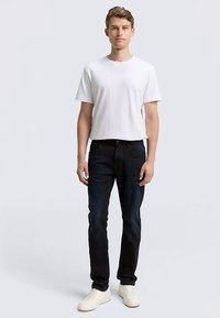 T-shirt en coton blanc associé à un jean en denim bleu foncé et des chaussures blanches. La tenue présente une coupe décontractée et un design classique, avec des détails minimalistes.
