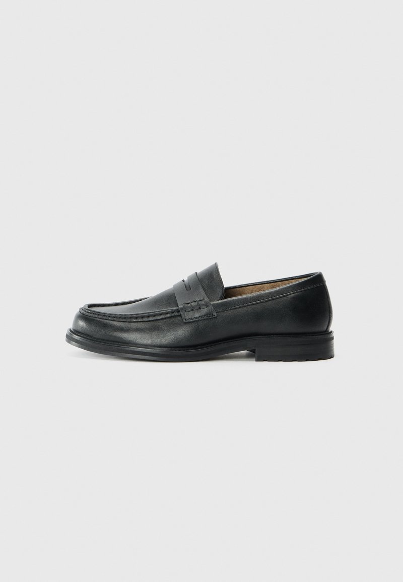 Mocassins en cuir noir au design classique, présentant un accent cousu sur le bout et une semelle en caoutchouc texturée et basse.