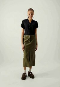 Black short-sleeved button-up shirt paired with an olive green knee-length skirt featuring a front slit. Brown platform shoes complete the outfit.