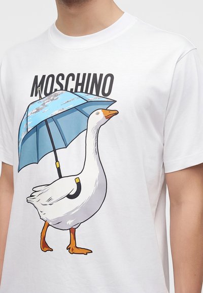 Λευκό T-shirt με γραφικό ενός λευκού χήνου που κρατά ένα μπλε ομπρέλα και τη λέξη "MOSCHINO" τυπωμένη από πάνω.