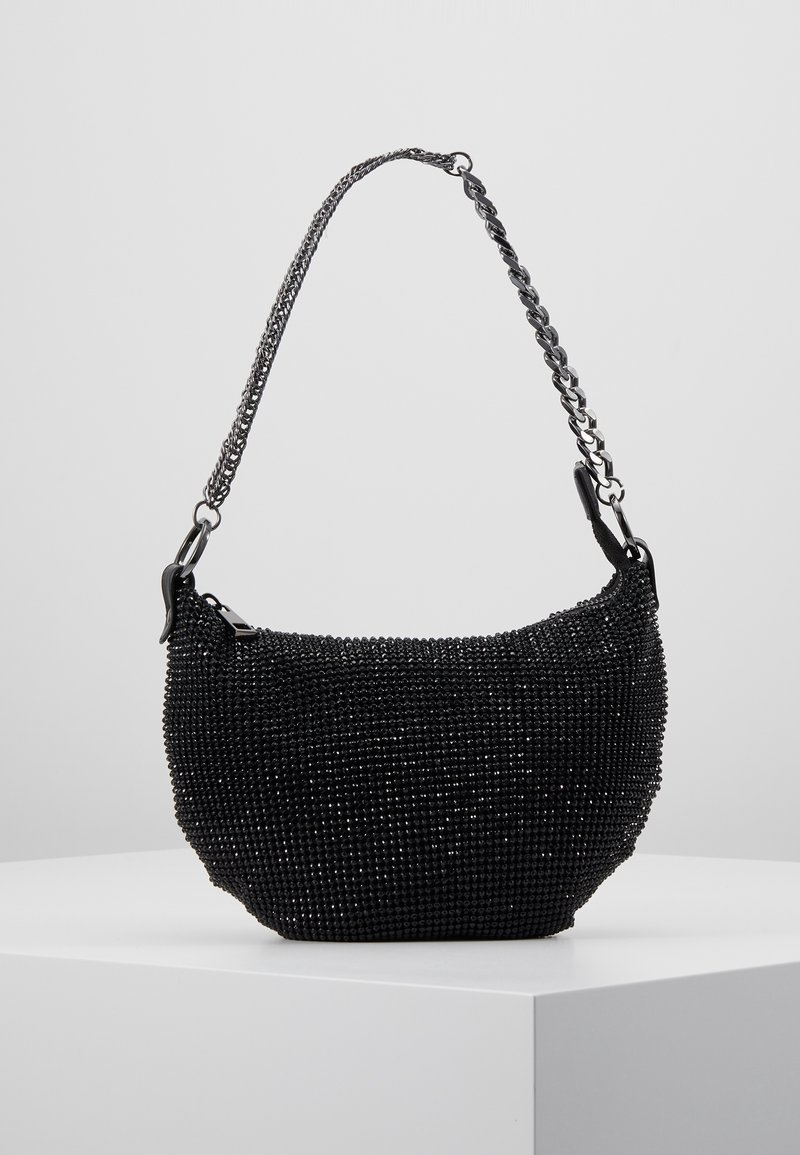 Petit sac à main noir avec des perles scintillantes et une courte chaîne en argent, présenté sur un socle blanc sur un fond uni.