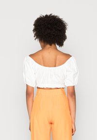 Top cropped branco sem alças, com mangas bufantes, combinado com calças laranja de cintura alta. Tecido suave, com detalhes elásticos na bainha.