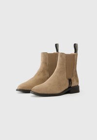 Bottes Chelsea en suède tan avec des panneaux élastiques sur les côtés, semelle plate et languettes contrastées à l'arrière. Bout arrondi et design minimaliste.
