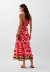 Abito maxi rosa a fantasia con un corpetto aderente e una gonna svasata, caratterizzato da un vivace design geometrico e un orlo verde a contrasto.