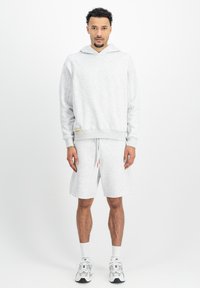 Svetlosivá mikina s kapucňou na sťahovanie, dlhými rukávmi a pruhovanými manžetami, kombinovaná s ukážkovými šortkami. Materiál odvádzajúci pot a minimálne logo.