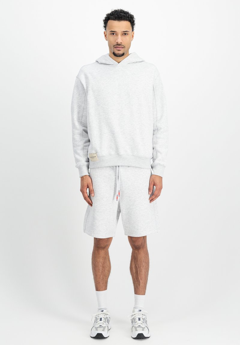 Svetlosivá mikina s kapucňou na sťahovanie, dlhými rukávmi a pruhovanými manžetami, kombinovaná s ukážkovými šortkami. Materiál odvádzajúci pot a minimálne logo.