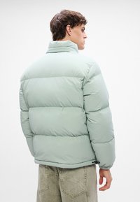 Svijetlo mentol zelena puffer jakna s visokim ovratnikom, s kvadriranim dijelovima, elastičnim manžetama i donjim rubom na vezanje za prilagodbu veličine.