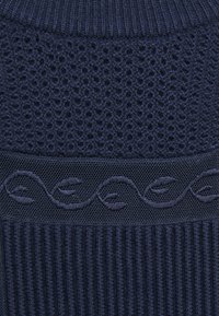 Marinblått strukturerat stickat tyg med öppen väv, ribbade sektioner och ett dekorativt broderat vågmönster längs sömmen.