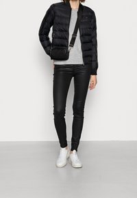 Svart puffig bomberjacka, grå stickad tröja, svarta läderbyxor och vita sneakers; liten svart axelväska med dragkedjedetalj.