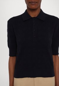 Polo a maniche corte blu navy con motivo testurizzato, colletto strutturato e patta con bottoni. Il tessuto sembra morbido e lavorato a maglia.