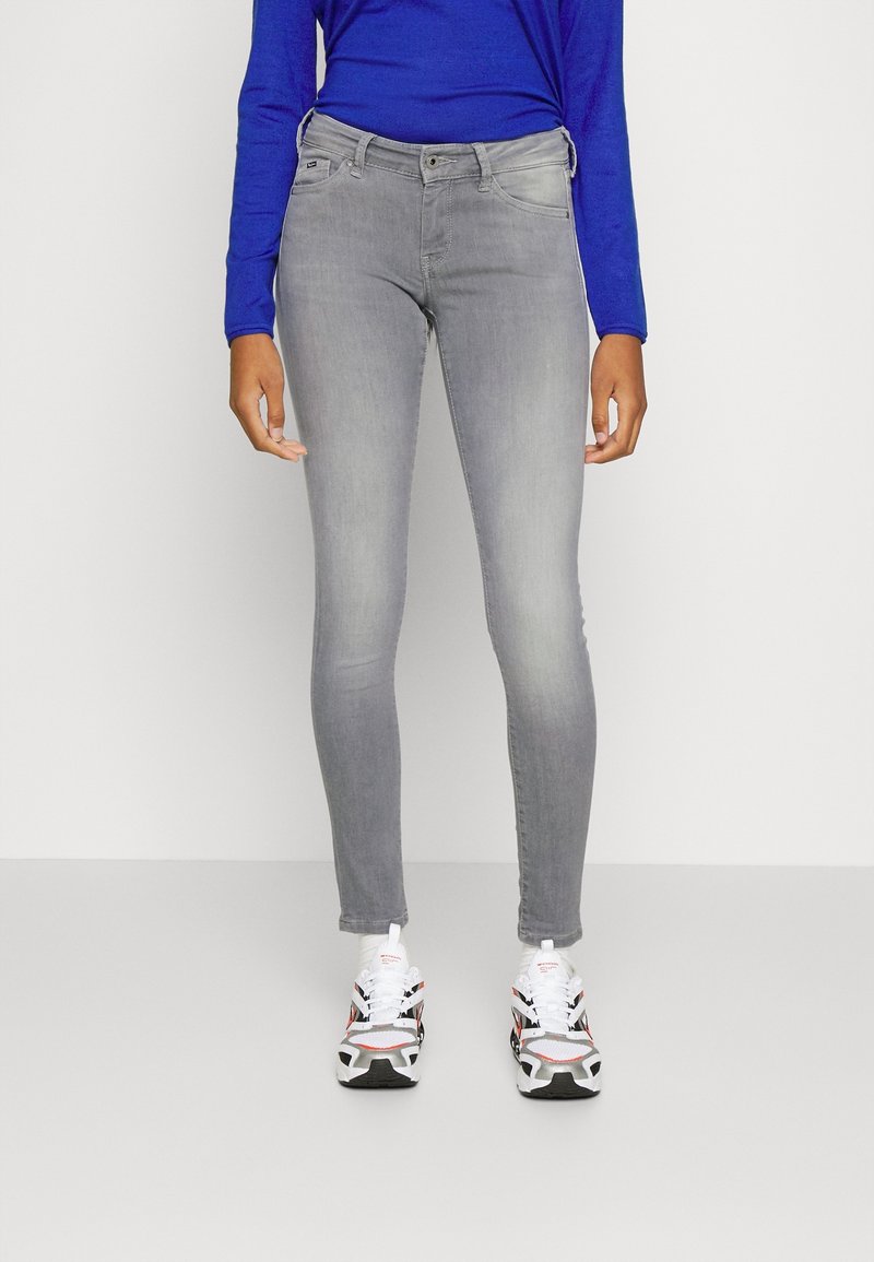 Jeans ajustados grises de mezclilla con un ligero desgaste, combinados con una camiseta de manga larga azul y zapatillas con un diseño estampado.