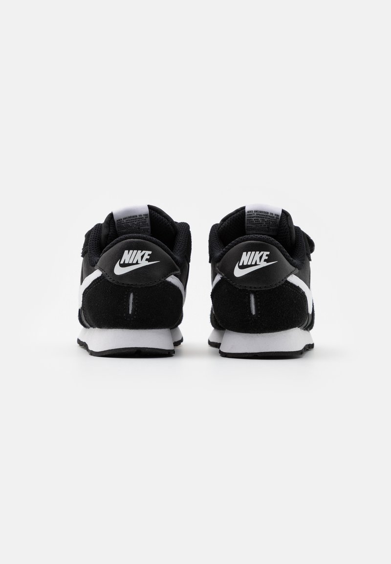 Zapatillas Nike negras con acentos blancos, materiales de ante y malla, tacón redondeado y logotipo prominente en la parte trasera. Diseño simple y atlético.