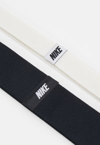 Nike headbands in black and white, made of soft fabric with texture, featuring a prominent logo tag stitched on each.