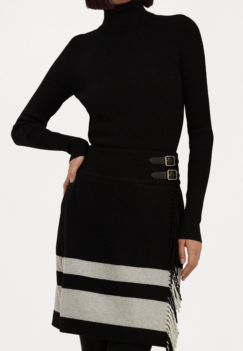 Svart ribbad polotröja i kombination med en svart minikjol med grå ränder och fransdetaljer, säkrad med dubbla spännen.