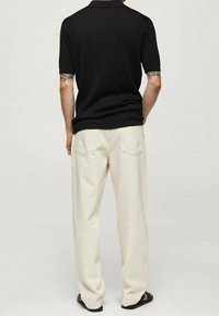 Černé krátké rukávy, žebrovaný polo shirt spárovaný s krémově bílými, volně střiženými kalhotami. Sandály dotvářejí outfit a vyjadřují minimalistic styl.