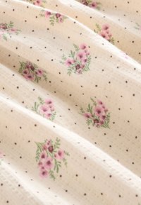 Tela color crema con pequeños ramos de flores rosas y puntos marrones dispersos, mostrando pliegues suaves y un patrón texturizado de punto.